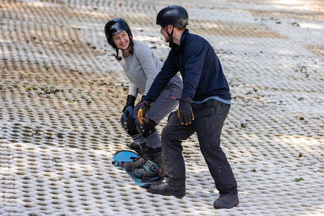 A lady on her snowboard with the instructor watching